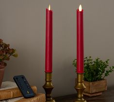 two red candles sitting on top of a wooden table next to a tv remote control