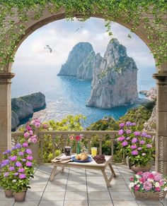 an outdoor table with flowers and fruit on it in front of a scenic ocean view