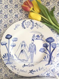 a blue and white plate with an image of a bride and groom on it next to tulips