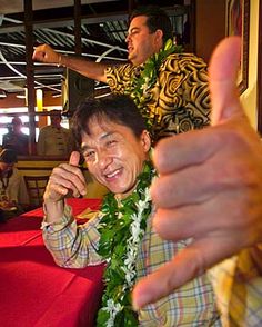 a man sitting at a table giving the thumbs up sign with another man standing behind him