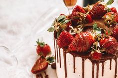 a cake with strawberries and chocolate drizzled on top, next to two wine glasses