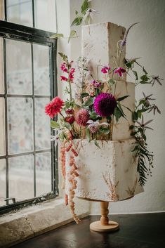 a tall white cake with flowers on it sitting in front of a window sill