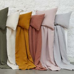 four different colors of pillows lined up against a white wall with one folded over the other