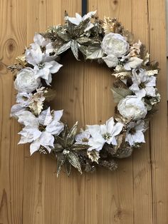 a wreath with white flowers and gold leaves on a wooden door hanger in front of a wood paneled wall