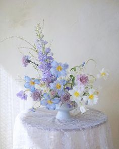 a white table topped with a blue vase filled with purple and yellow wildflowers