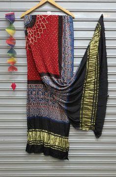 A Beautiful Gaji silk dupatta with the combination of two different crafts Bandhani and Ajrakh. Bandhani is a traditional form of tie-dye native to Gujarat and Rajasthan. It is a highly skilled technique where the fabric is elaborately tied & dipped in dyes and threads are removed leaving behind tiny circles characteristic of Bandhani. Ajrakh derived from the Persian to mean Indigo, a color hard to miss among the geometric and floral patterns of Ajrakh work. Ajrakh is a block-printing technique Dupatta For Navratri, Gaji Silk Dupatta, Gajji Silk Dupatta, Bandhani Dupatta, Textile Bag, Saree Blouse Designs Latest, Blouse Designs Latest, Silk Dupatta, Vintage Textiles