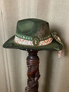 This is a custom weathered hat with incredible detail.  Green felt hat with band of white fabric w orange flowers. Green brocade hat band.  Victorian picture frame.  Chain at bottom.  Hat has been wood burned a beautiful scroll design.  Vintage clock medallion.  Authentic Turkey feathers in back.   Adjustable band inside to fit any size. Vintage Handmade Hat Band For Western-themed Events, Vintage Handmade Hats For Country Events, Vintage Felt Hat For Western-themed Events, Handmade Adjustable Vintage Top Hat, Handmade Vintage Felt Hat For Country Events, Handmade Vintage Hat Bands For Kentucky Derby, Handmade Vintage Fedora For Kentucky Derby, Handmade Vintage Fedora For Country Events, Vintage Felt Hat For Country Events