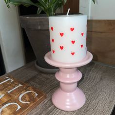 a white candle with red hearts on it sitting on a table next to a potted plant