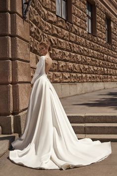 a woman in a white wedding dress is standing on the steps near a brick building