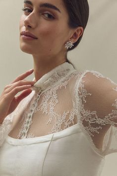 a woman in a white dress is posing with her hands on her chest and wearing earrings