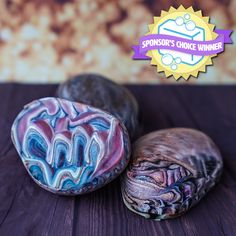 three different colored rocks sitting on top of a wooden table next to a purple ribbon