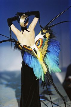 a woman in a black dress with feathers on her head and hands behind her back