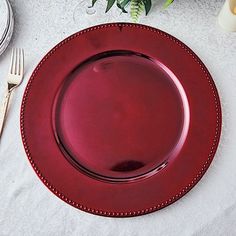 a red plate sitting on top of a white table cloth next to a knife and fork