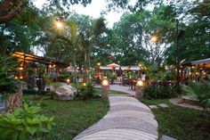 an outdoor area with tables and umbrellas in the evening light, surrounded by lush greenery