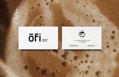 two white business cards sitting on top of a brown liquid filled surface with drops of water