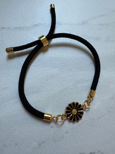 a black cord bracelet with a gold flower charm on it's end and two small beads attached to the clasp