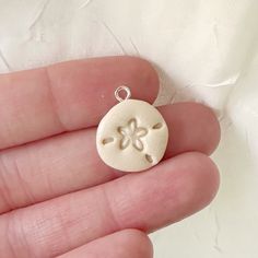 a hand holding a small white ceramic pendant