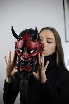 a woman holding up a red mask with horns