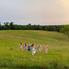 four girls are walking in the grass with their arms around each other and one girl is flying a kite