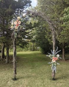 an arch made out of branches with flowers on it in the middle of a field