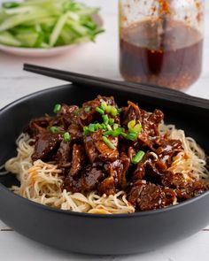 a bowl filled with beef and noodles next to chopsticks on a table top