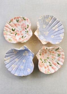 four seashells with flowers painted on them are arranged in a circular pattern, one is blue and the other is pink