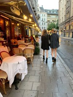 two women walking down the street in front of tables and chairs