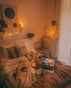 a laptop computer sitting on top of a bed covered in blankets and pillows next to a window