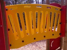 a yellow plastic play structure with red and yellow bars on the top, in a park