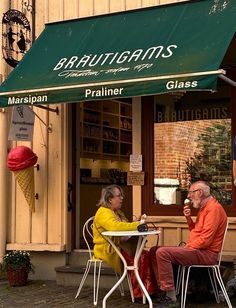 two people sitting at an outdoor table in front of a building with green awning