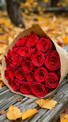 a bouquet of red roses sitting on top of a wooden bench in the fall leaves