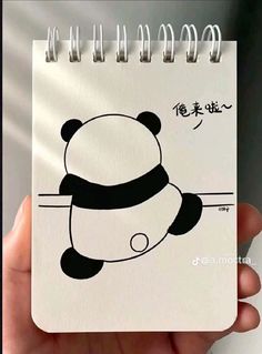 a hand holding a spiral notebook with a drawing of a panda bear on the cover