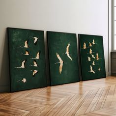 three framed paintings with birds flying in the air on a wooden floor next to a window