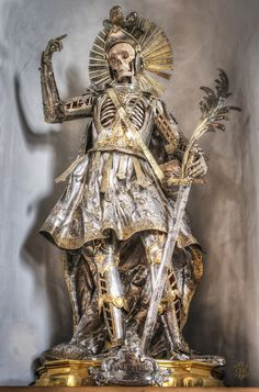 a statue of a skeleton in armor holding two swords and wearing a crown with gold accents