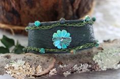 a green leather bracelet with flowers and beads on the side, sitting on a piece of wood