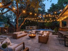 an outdoor patio with seating and string lights strung over the fire pit, surrounded by trees