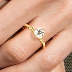 a woman's hand with a yellow gold ring and a white diamond on it