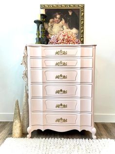 a pink dresser sitting on top of a white rug next to a painting and vase