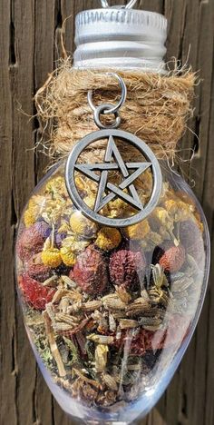 a glass jar filled with different types of flowers and herbs hanging from a string on a wooden fence