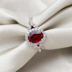 a red stone ring sitting on top of a white satin bowknott with diamonds around it