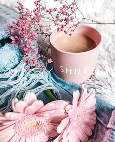 pink flowers are sitting next to a cup of coffee on a blue and white blanket