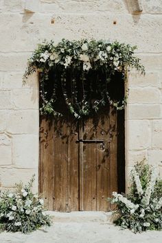 an old wooden door with white flowers on it and greenery hanging over the doors