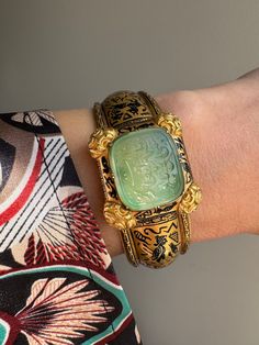 "This exquisite  archeological-revival bangle is attributed to Robert Phillips, circa 1865. The hinged bangle is decorated with Egyptian hieroglyphs in glossy black enamel culminating in a jade intaglio with a covered compartment to the reverse. \"ذات تو مظهر انعام سبحانی باد\", written in Farsi, it translates to, \"May your essence be a manifestation of divine blessings.\" A beautiful sentiment of well-wishing and hope for a positive and spiritually enriched existence. Hand fabricated in 15 karat gold, this bangle fits a petite 6\" wrist. A rare and wonderful jewel.    Weight: 28.1 grams Markings: none  Measurements: 6\" interior circumference, 1\" widest point (face) Notes: some losses to the enamel as shown" Traditional Jewelry With Historical Design For Collectors, Ceremonial Antique Yellow Gold Cuff Bracelet, Antique Yellow Gold Cuff Bracelet For Ceremonial Occasions, Luxury Engraved Bracelets For Ceremonial Occasions, Traditional Ceremonial Intaglio Jewelry, Antique Intaglio Ceremonial Jewelry, Antique Intaglio Jewelry For Ceremonial Occasions, Antique Ceremonial Intaglio Jewelry, Traditional Carved Yellow Gold Jewelry