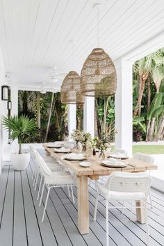 an outdoor dining area with white wicker chairs and wooden table