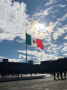 the flag is flying high in the sky above some buildings and people are walking around