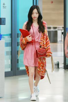 a woman in a pink dress is walking through an airport with her handbag on her hip