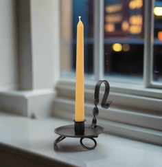 a lit candle sitting on top of a black plate next to a window sill