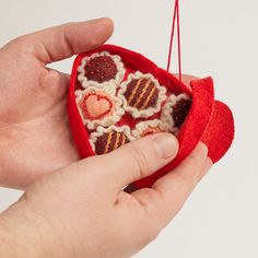 a hand holding a red heart shaped ornament with hearts on it's side