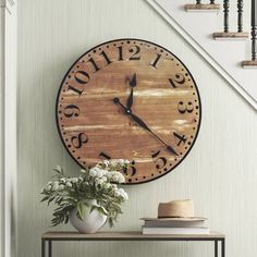 a clock on the wall above a table with flowers and books in front of it