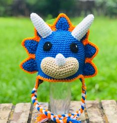 a crocheted blue and orange animal hat on top of a wooden table with grass in the background